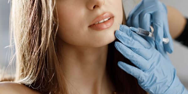 Closeup of doctor's hands in gloves with syringe near female face. Portrait of beautiful caucasian woman with white towel on her bodu. Girl receiving beauty injection.